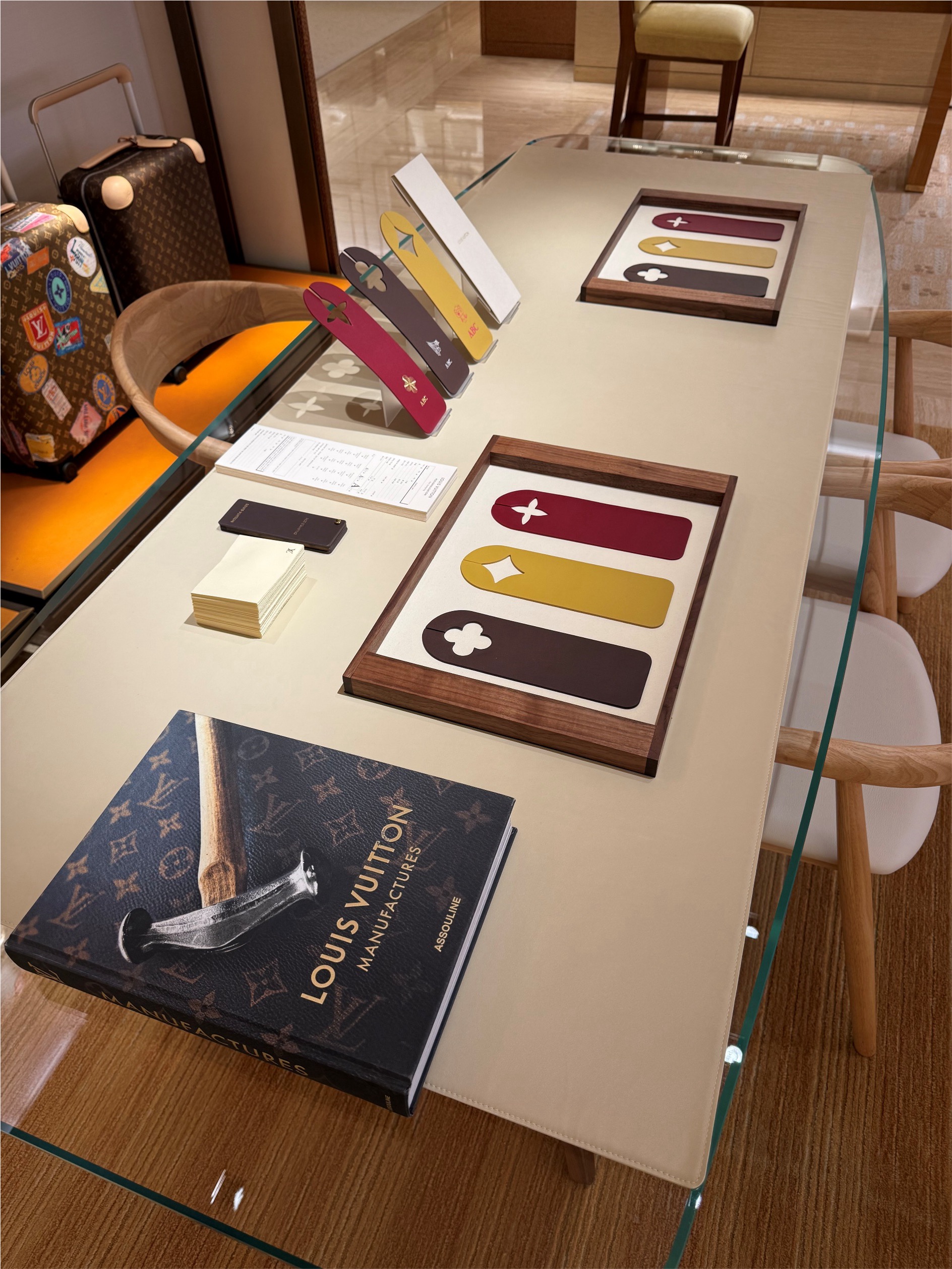 Detail of Louis Vuitton leather tags in walnut trays and on an angled stand, beside a Louis Vuitton Manufactures book