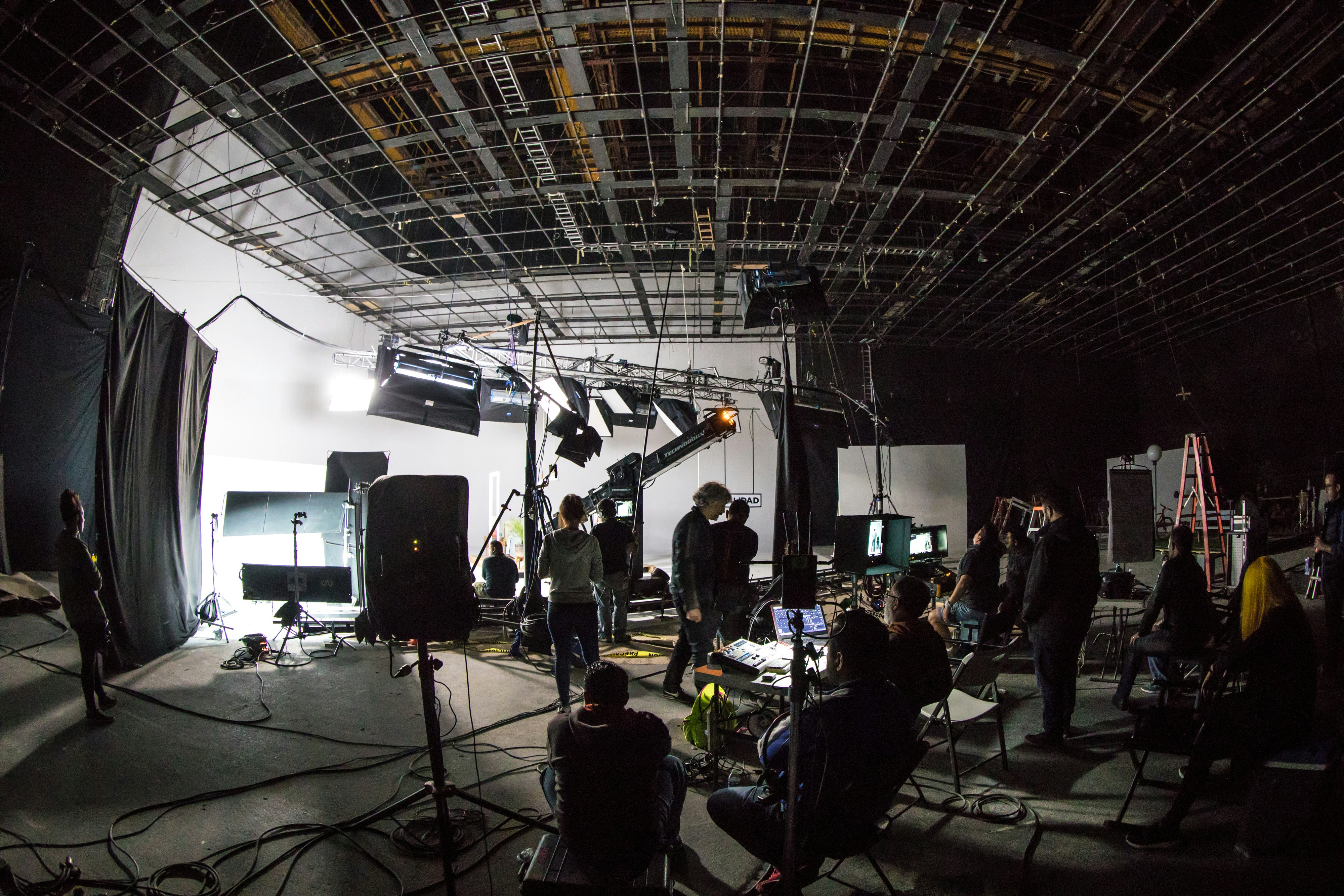 Production crew working on a lit film studio set with camera crane, lighting rig and monitors