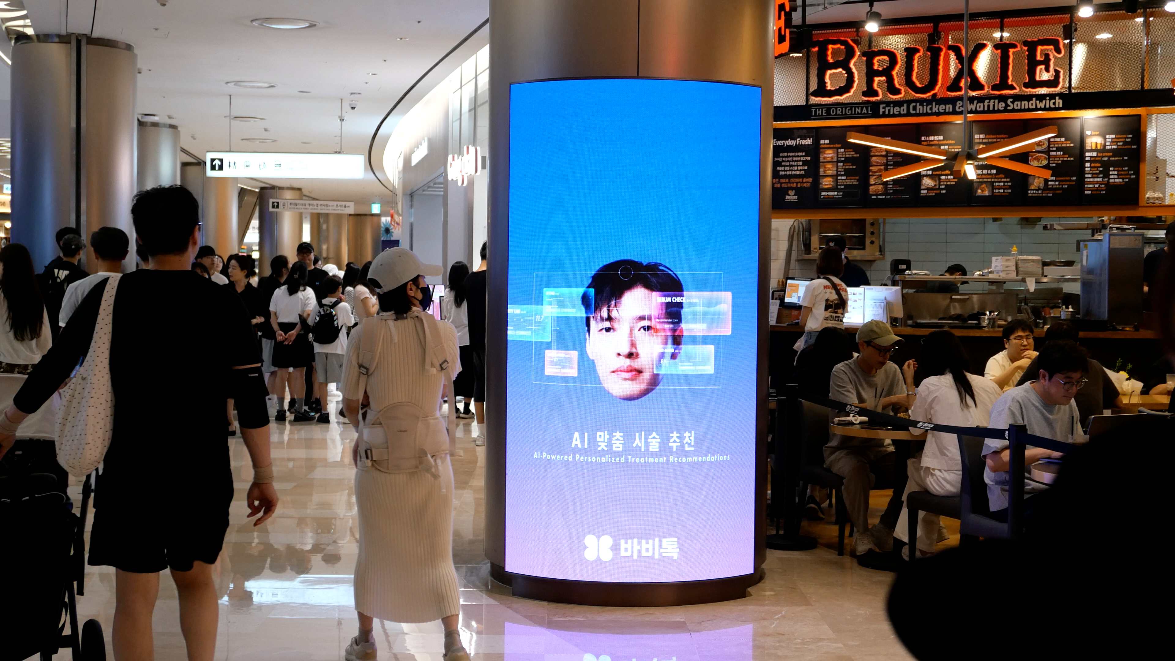 BABITALK AI treatment recommendation creative on a curved digital column beside a food hall, Lotte World Mall