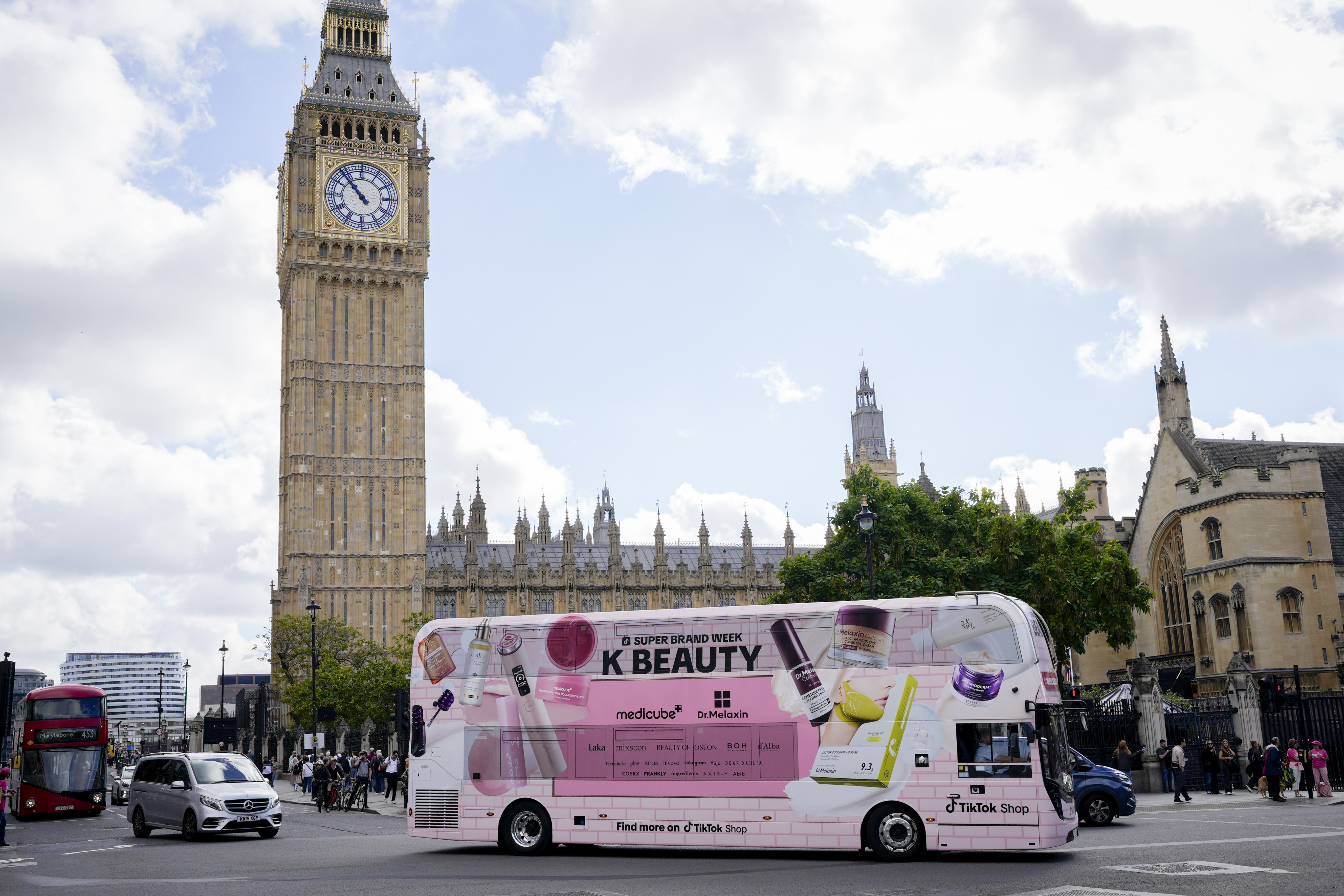 Pink TikTok Shop K-BEAUTY double-decker bus passing Big Ben and the Houses of Parliament, London