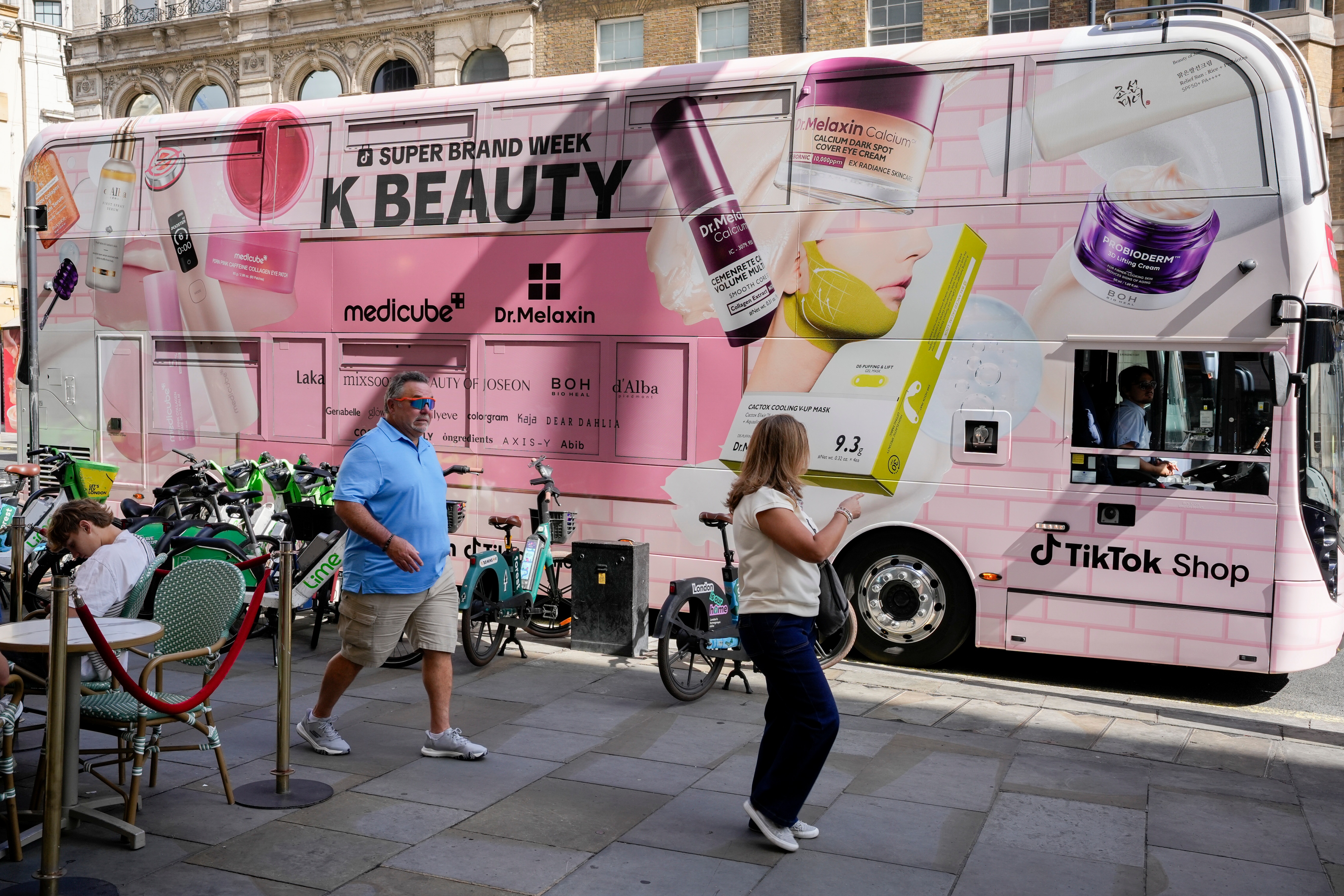 Pedestrians walking past the K-BEAUTY bus wrap on a London street