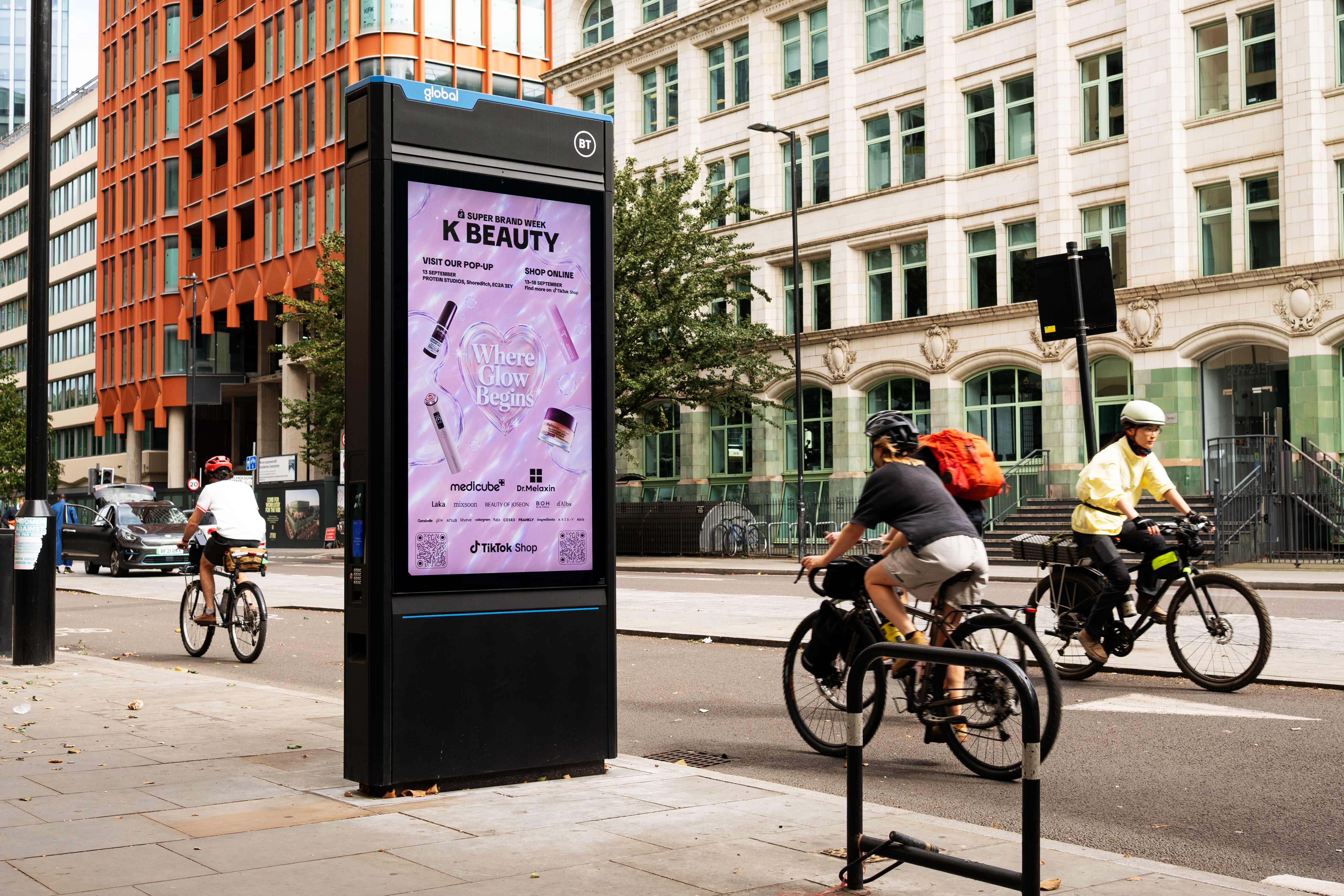 TikTok Shop K-BEAUTY Super Brand Week creative on a London StreetHub screen as cyclists pass