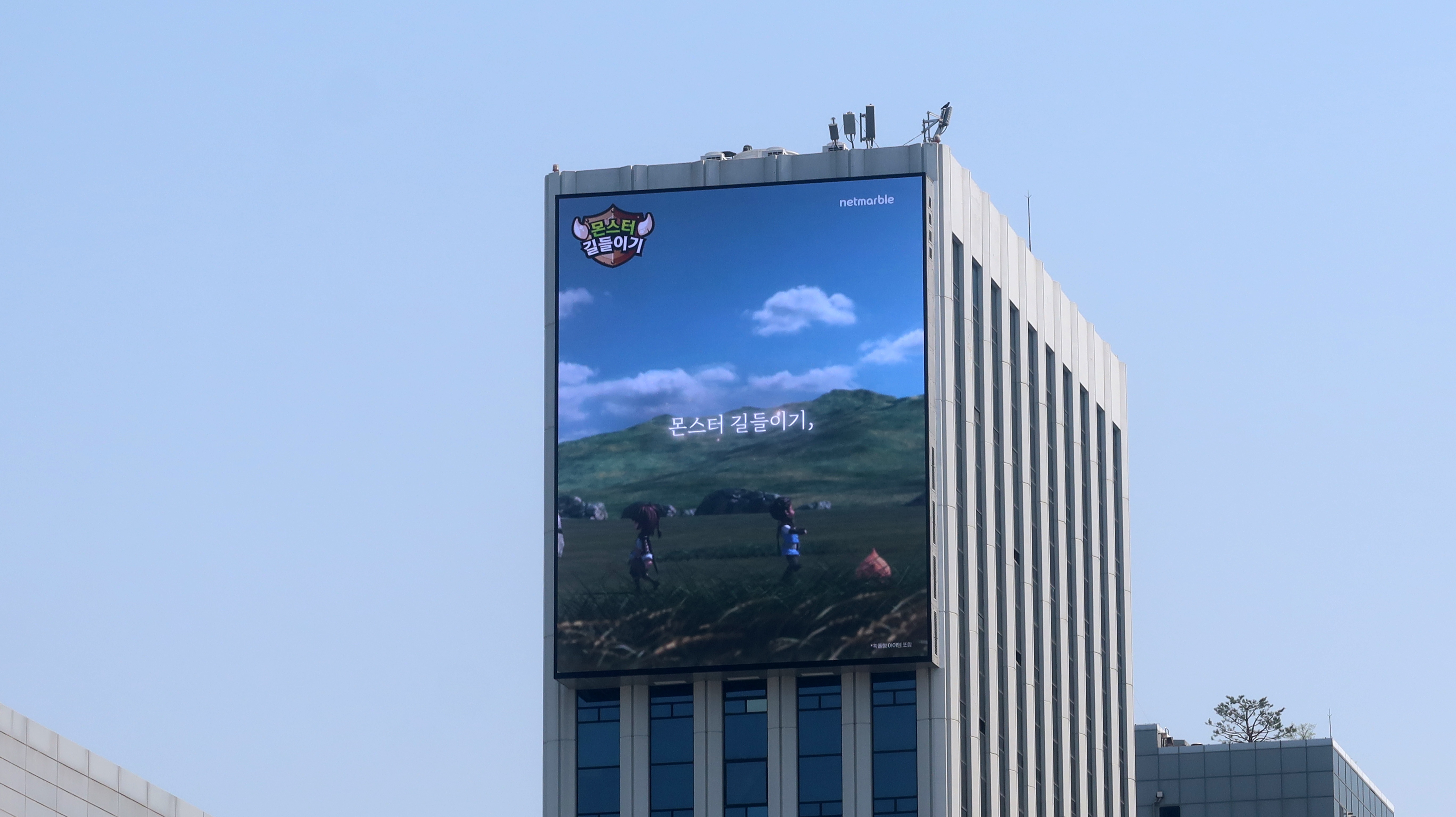 Monster Taming creative from the MONGIL: STAR DIVE campaign on a large screen at the top of a Seoul office tower