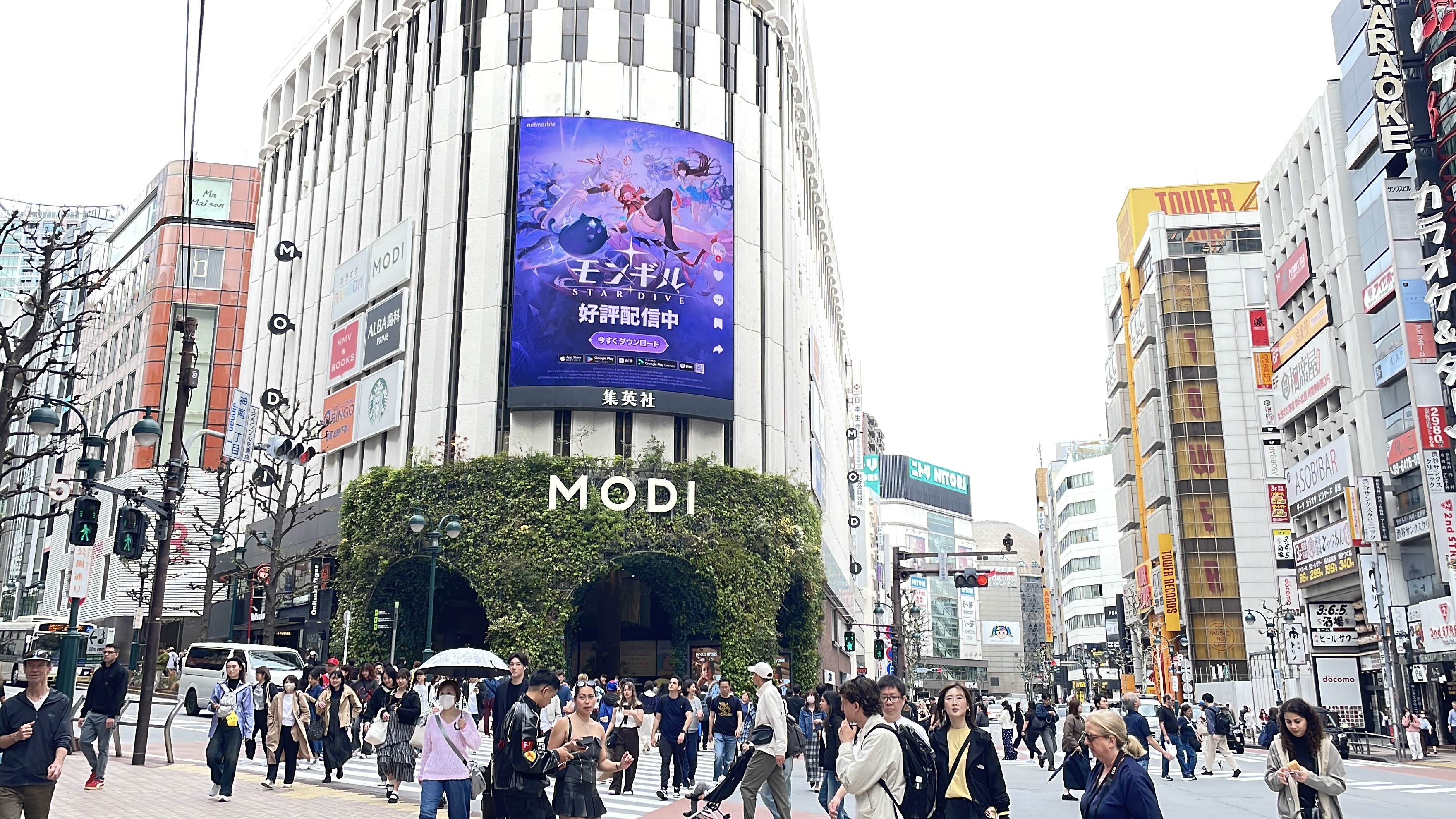 MONGIL: STAR DIVE Japanese creative on the curved screen above the MODI building as crowds cross the street, Shibuya, Tokyo