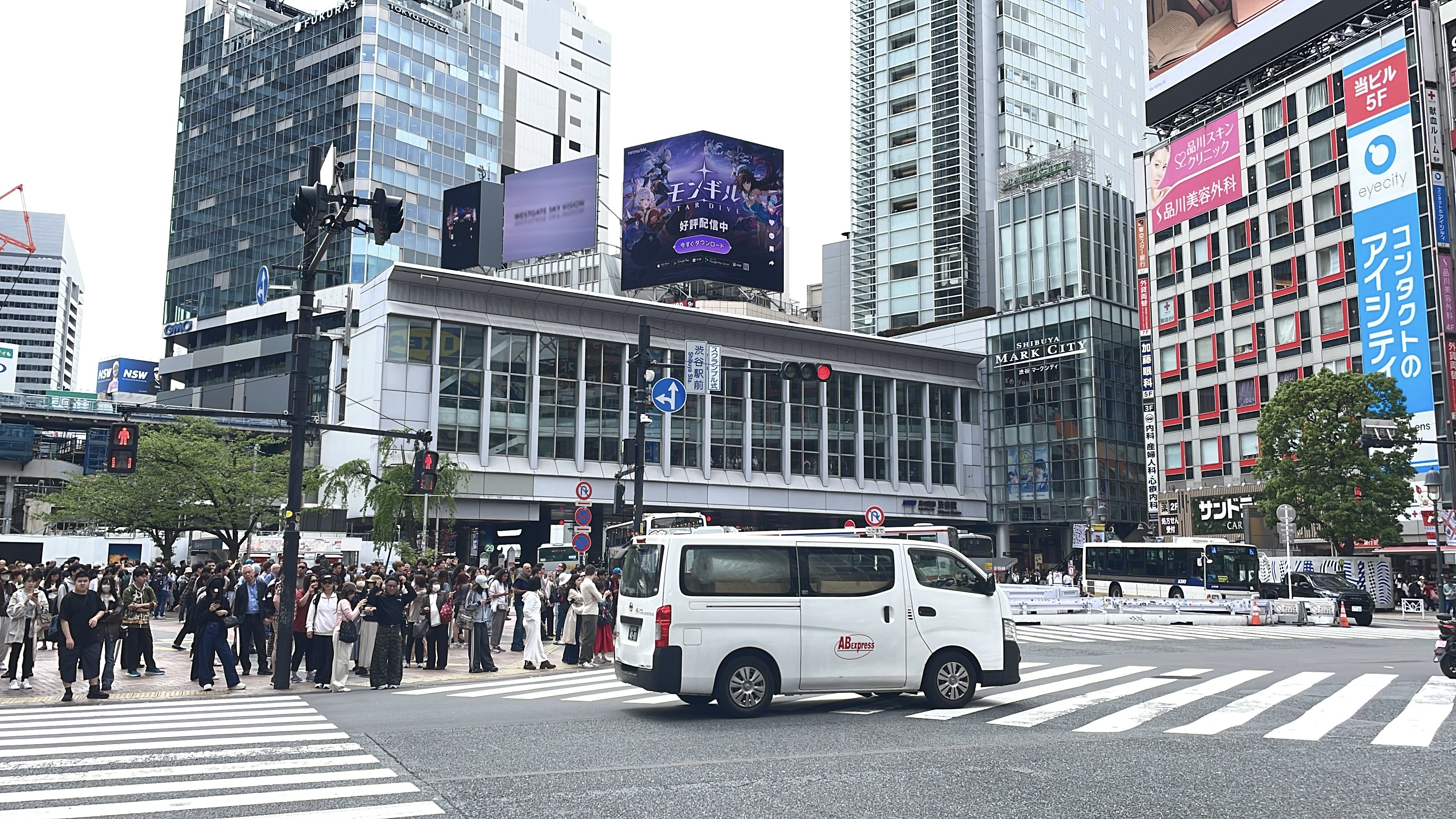 Crowds waiting at the Shibuya crossing beneath a rooftop screen running the Japanese MONGIL: STAR DIVE creative, Tokyo