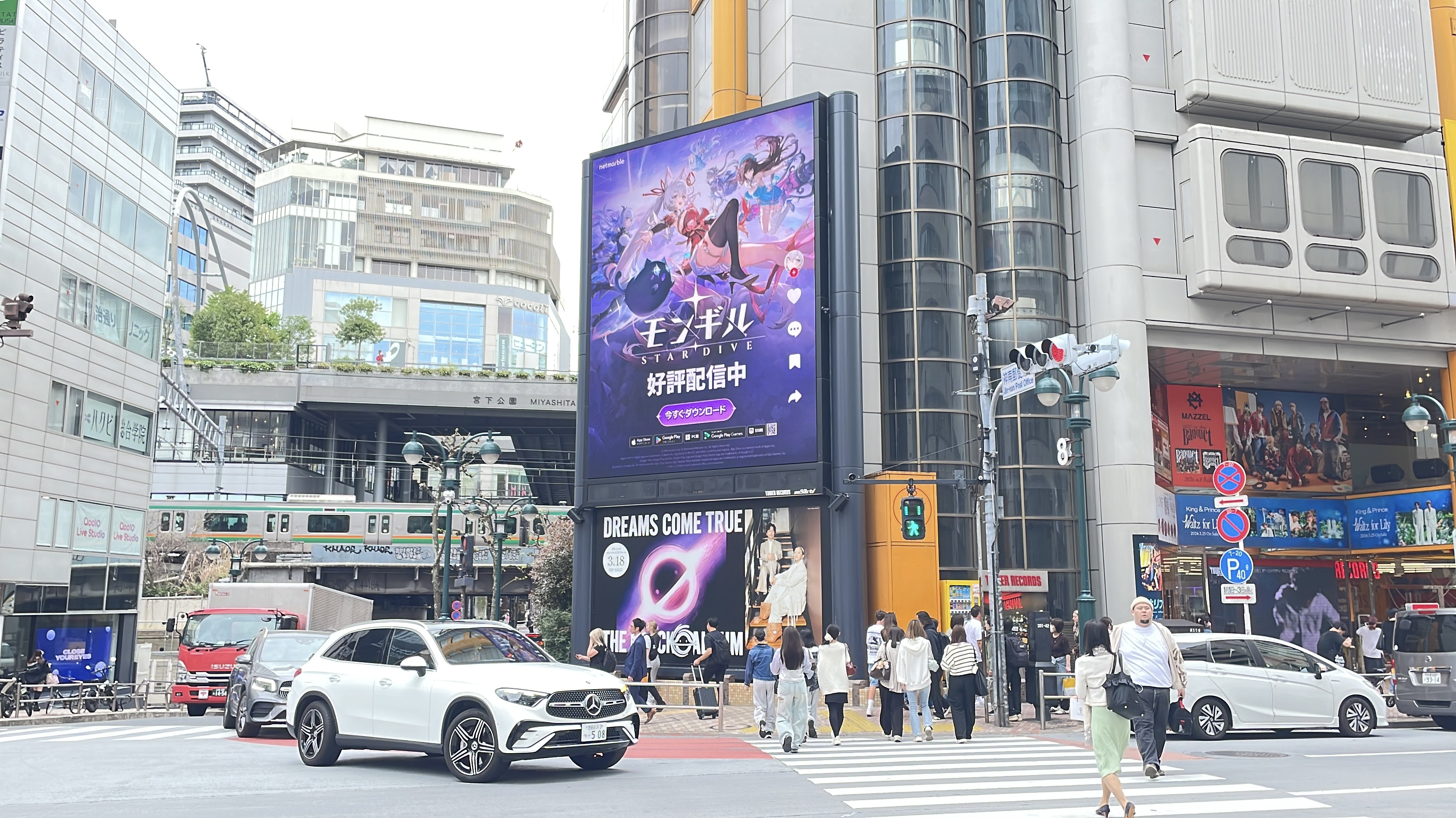Pedestrians crossing in front of the Tower Records Shibuya screen showing the Japanese MONGIL: STAR DIVE creative, Tokyo