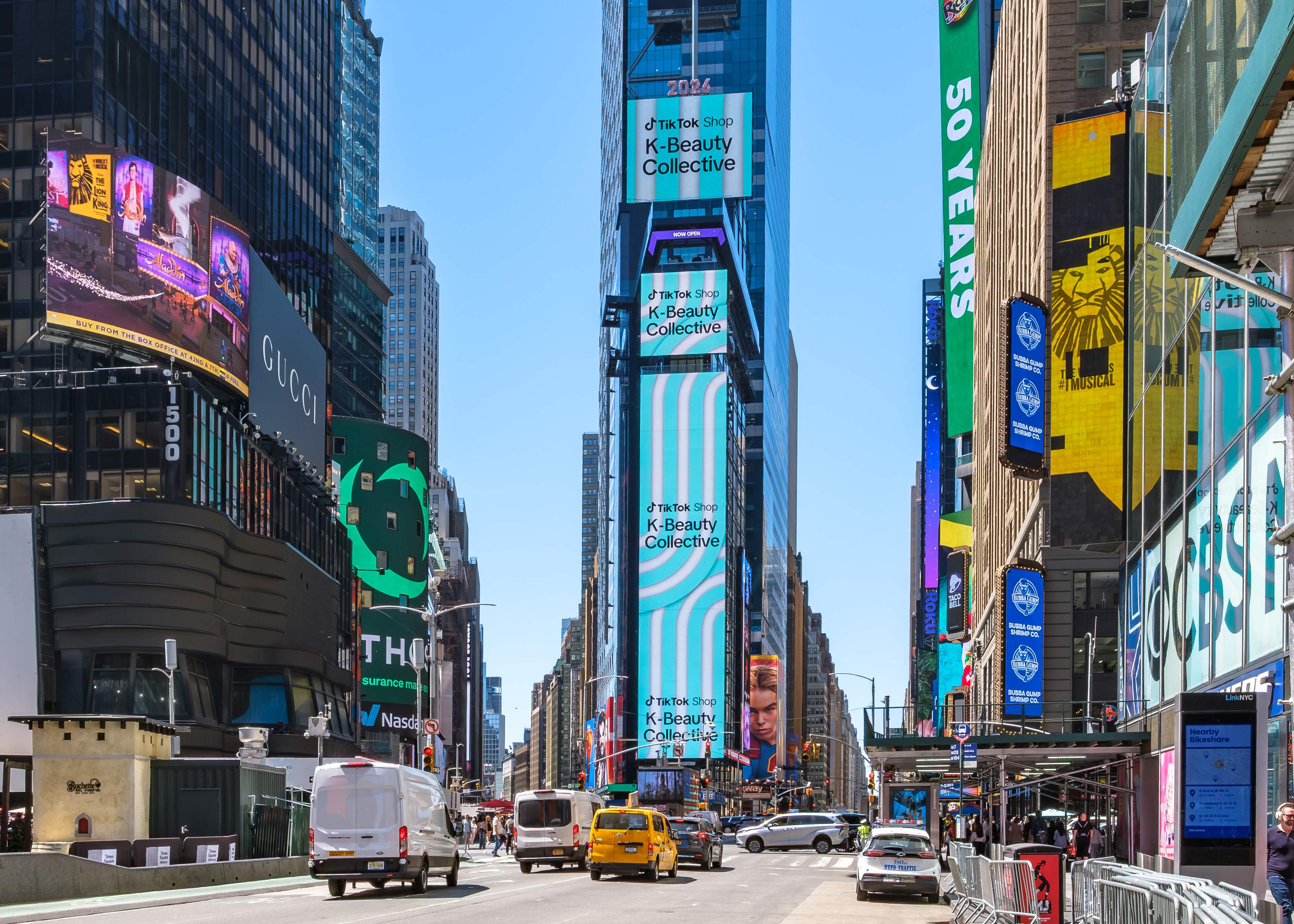 Street-level view up Seventh Avenue to the full vertical TikTok Shop K-Beauty Collective structure in Times Square